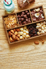 Top view of assorted nuts and cereal in a box with homemade chocolate bars and bottle of milk on wooden table. Healthy kid's breakfast concept.