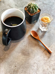 Black coffee cup with wooden spoon , green cactus , brown sugars in glass on cement background. Love coffee, copy space