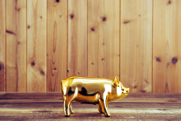 金色の豚の貯金箱と木目の壁 - obrazy, fototapety, plakaty