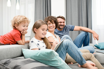 Joyful family of four gathered together in cozy living room and enjoying each others company, pretty little girl drawing picture with pencil