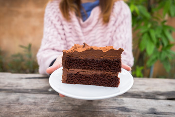 Close-up of woman's hand holding plate of chocolate cake in outdoor garden in winter season. Concept sweets enjoy eating.