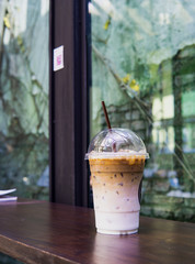 Ice coffee latte in takeaway cup on wood table. Takeaway ice latte in plastic cup with straw on wood table. Cafe shop background with ice latte on wood table