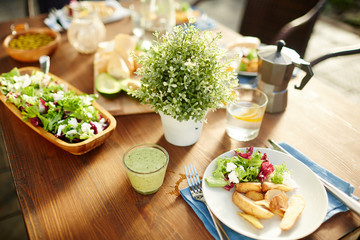 Glass of fresh vegetable smoothie, salad and roasted potatoes on plate, homemade lemonade and other food served on table