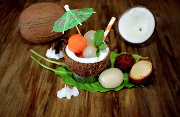 Tropical fruits: longan, rambutan and papaya ball-shaped pieces are lying in a coconut. Cocktail ingredients
