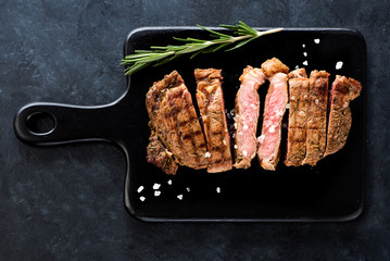 Slices Steak Ribeye with rosemary and salt on a black cutting board