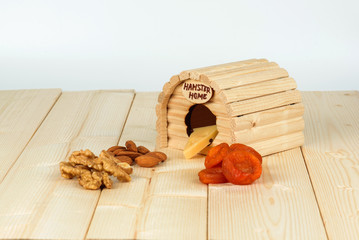 A wooden house and a treat for a hamster. Nuts, dried apricots and cheese.