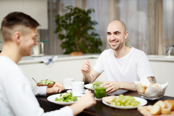 Fototapeta na wymiar Happy young homosexual couple sitting by table in the kitchen and having breakfast