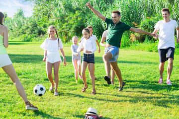 Two friendly families with children playing football in nature at summer