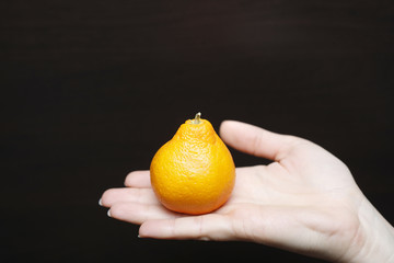 Tangerine close up. Woman holding fresh tangerine. Unusual tropical fruit looks like pear.