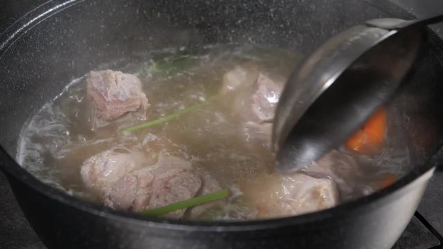 traditional beef broth with vegetable, bones and ingredients in pot, cooking recipe. Soup in a cooking pot with ladle on dark stone background. Top view