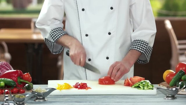Chef cutting a tomato. Man with knife preparing food.