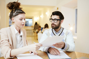 Fototapeta premium Serious employee showing paper or contract to his colleague during work in cafe