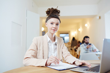 Contemporary young professional accountant sitting by workplace, working with documents and...