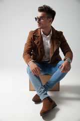 young fashion man sitting on a box and looks away