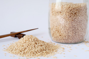 pink rice in a glass jar with a lid yoke, brown wooden sticks, white background