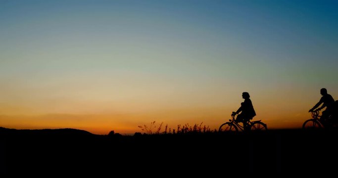 Side shot - Silhouette of family riding bikes in beautiful summer evening.
