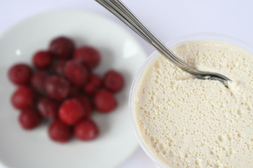 spoon stands in a glass with a thick sour cream, red berries, white background