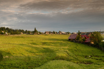 a typical Russian village, wooden houses, the smoke from the chimney, blue sky, green fields