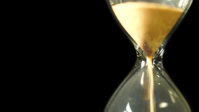 Sand running through the bulbs of an hourglass measuring the passing time in a countdown to a deadline, on a black background with copy space for your text.