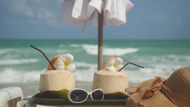 Tropical fresh coconut cocktails in beach cafe with hat, sunglasses, umbrella on a turquoise sea background. slow motion. 192x1080