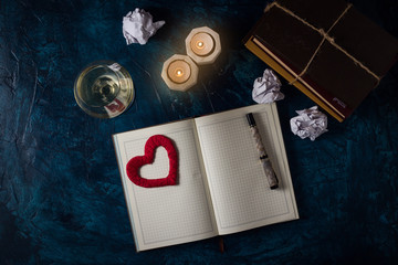 Glass of White Wine, Clear Diary, Pen, Candles, Crumpled Paper, Heart, A stack of books on a dark blue background. Romantic concept. Copy space. Flat lay, top view