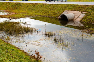 Concrete culvert pipe hole system draining sewage water near the puddle. Environmental disaster - obrazy, fototapety, plakaty