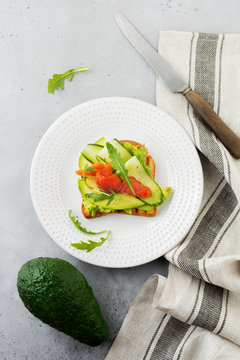 Open toast with trout, salmon, avocado, cucumber and arugula on wooden stand on gray concrete background. Selective focus. Top view. Copy space