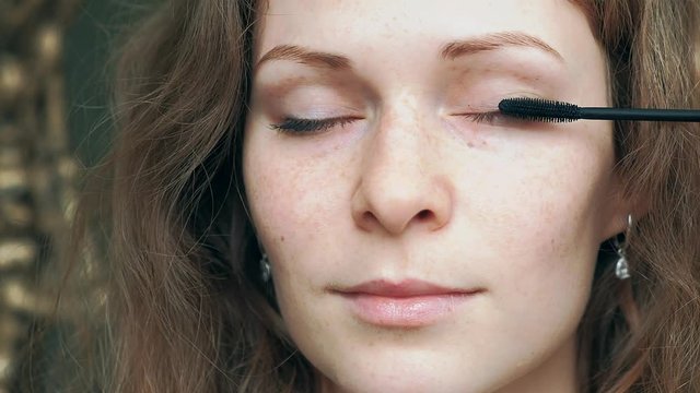 Eye in macro footage of young woman applying mascara on eyelashes