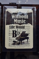 Sheet of paper with musical pun on life without music behind reflecting shop window.