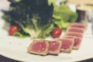 Close up of rare seared Ahi tuna slices with fresh vegetable salad on a plate. Top view from above horizontal