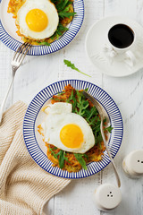 Fried egg with potato pancake, arugula and avocado on ceramic plate for breakfast on white wooden table background. Selective focus. Top view. Copy space.