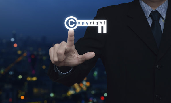 Businessman pressing copyright key icon over blur colorful night light city tower, Copyright and patents concept