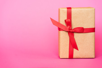 Gift in kraft box with a red bow on a pink background. The concept of St. Valentine's Day, weddings, birthday, New Year, Christmas holidays