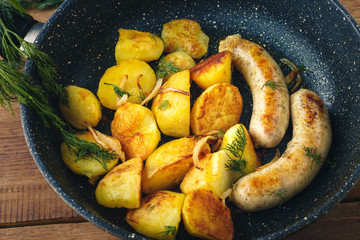 Fried sausages with baked potatoes, in a frying pan. Top view