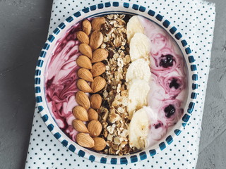Healthy food - berry smoothie and muesli made from oatmeal, almonds, banana and blueberries, in a beautiful plate on a gray table, close-up, top view