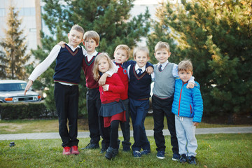 Happy school children in uniform and with backpacks holding hands and jumping in the park, back to school