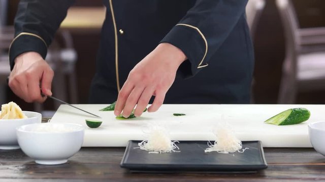 Chef slicing a cucumber. Fresh vegetable on cutting board.