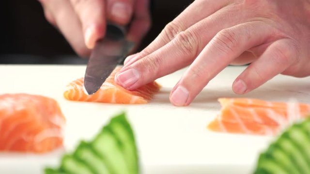 Hands slicing fish close up. Raw salmon on cutting board.