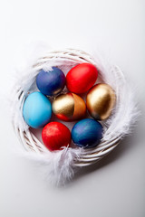 Eggs painted in various colors arranged with feathers in twig wreath on white background. Easter traditions concept.