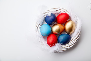 Eggs painted in various colors arranged with feathers in twig wreath on white background. Easter traditions concept.