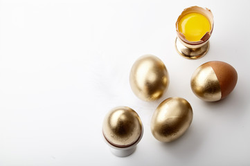 Eggs painted golden with yolk in egg stand on white background. Easter tradition concept, copy space