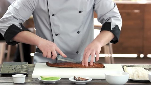 Sushi chef cutting smoked eel. Man preparing food, fish.
