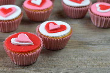 CUPCAKES decorated with hearts arranged on wooden background
