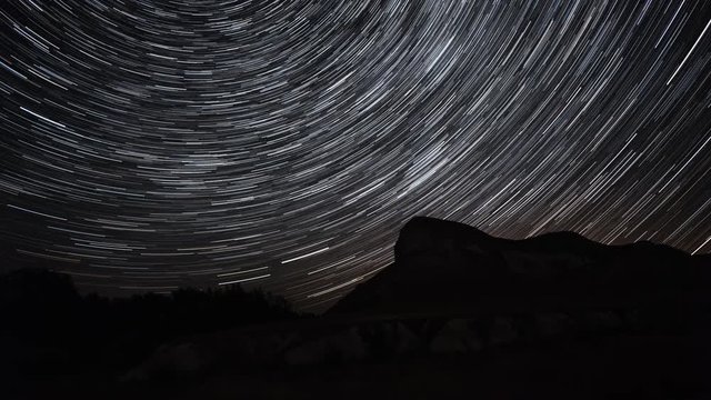 Beautiful star trails time-lapse over the hills. Polar North Star at the center of rotation. Lateral light from the full moon on the chalk hills. 4K resolution.