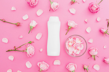 Roses flowers buds with petals and shampoo on pink background. Beauty female concept. Flat lay, Top view.