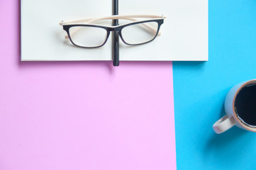 Eye glasses on open notebook on pink and blue background with copy space
