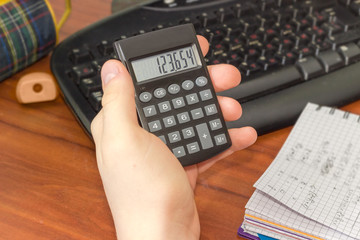 Electronic calculator in the hand of schoolboy over the desktop