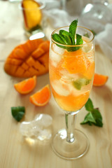 Fototapeta premium Sparkling cocktail with mango pieces, ice cubes and mint in a wineglass