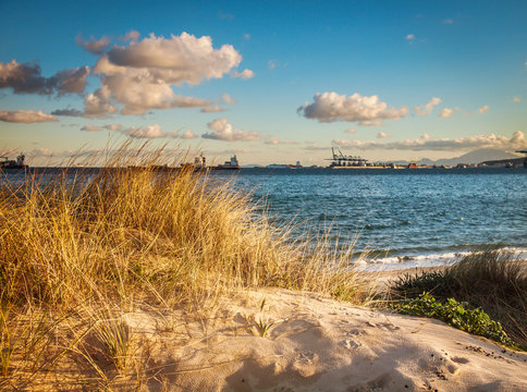 Algeciras, Spain. sand dune with sea grass and clouds with ship in the background