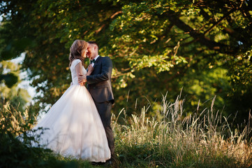 Newly married couple enjoying each other's company and kissing in the forest at sunset on their wedding day.